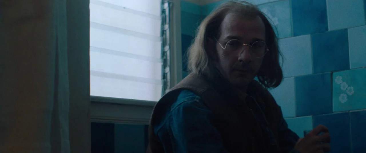 Honey Boy (2019) movie still: medium — A bathroom interior with blue and white tiled walls and a frosted window. A man with receding brown hair and…