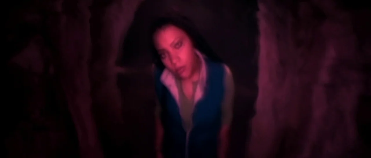 Bones movie still: medium — A dark, narrow passageway with uneven stone walls surrounds the subject. A woman stands in the middle, looking upward…