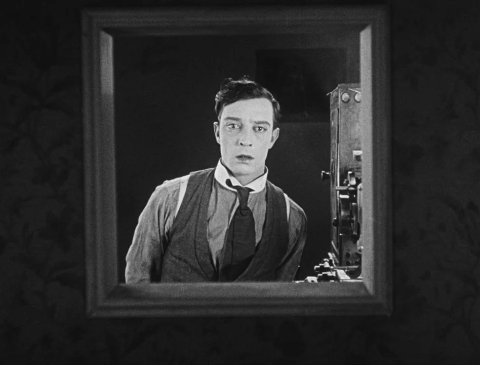 Sherlock Jr. (1924) movie still: medium — A dark, cramped interior space features a man reflected in a mirror frame. The man stands beside a…