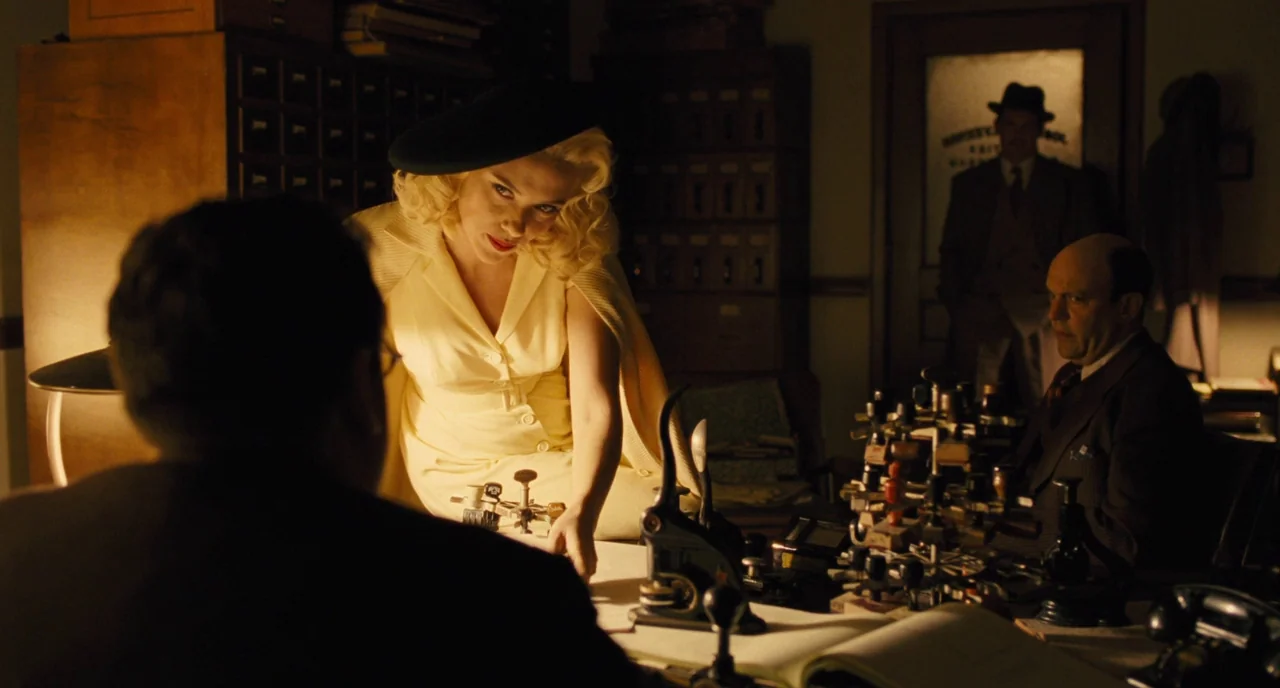 Hail, Caesar! (2016) movie still: medium — A dimly lit room filled with wooden filing cabinets and period-appropriate desk equipment. A woman in…