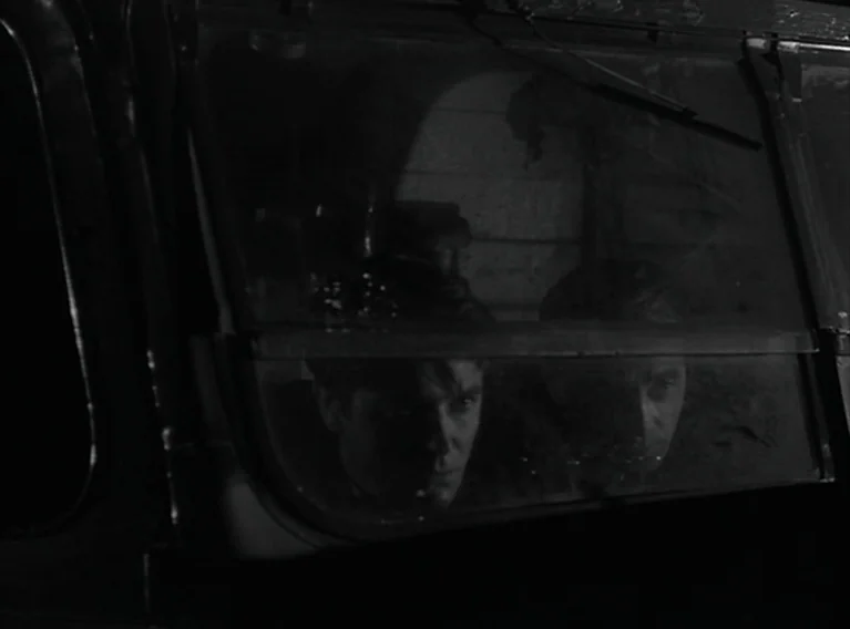Head Against The Wall (1959) movie still: medium — Two men sit inside the dark cabin of a vehicle at night. They peer out through the glass window,…