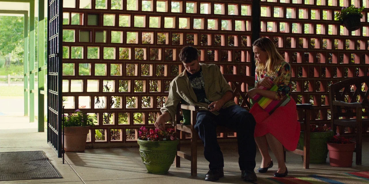 The Death of Dick Long (2019) movie still: medium — A patio area features a distinctive geometric brick screen wall and various potted plants. A man…