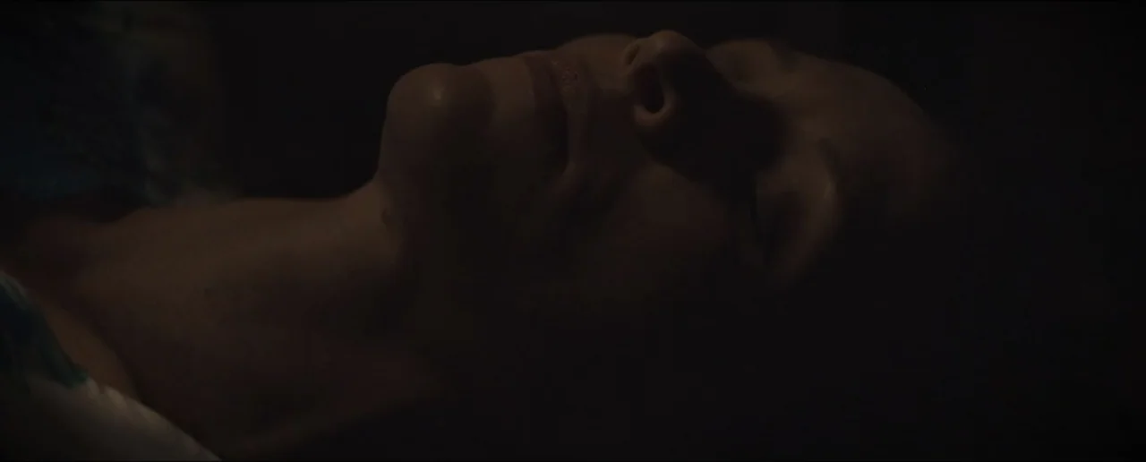 Hostages (2017) movie still: closeup — A dark, dimly lit indoor setting provides a minimal backdrop for a person. A woman lies with her eyes closed…