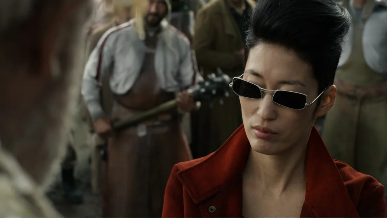 Mortal Engines (2018) movie still: medium — A crowded outdoor market features figures in weathered clothing and various handheld tools. A woman in a…