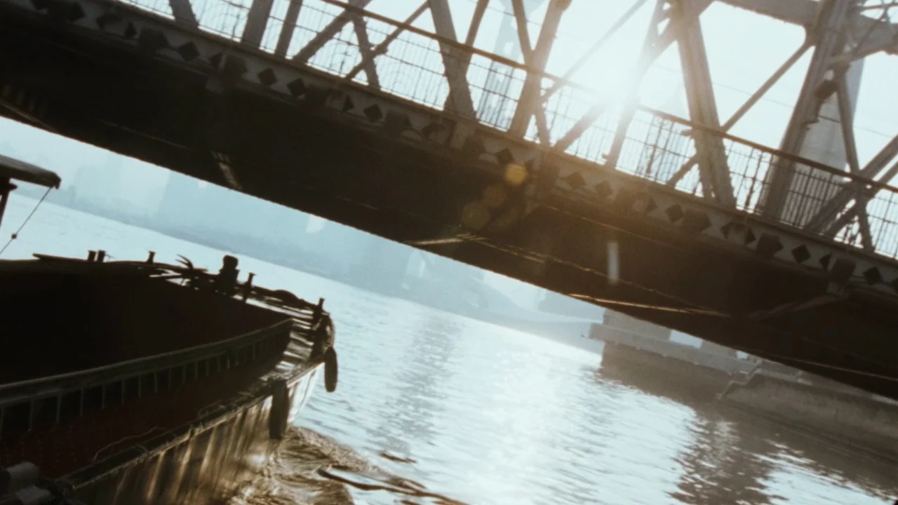 Suzhou River (2000) movie still: wide — A metal bridge spans across a wide river with a barge passing underneath it. Hazy city buildings are faintly…