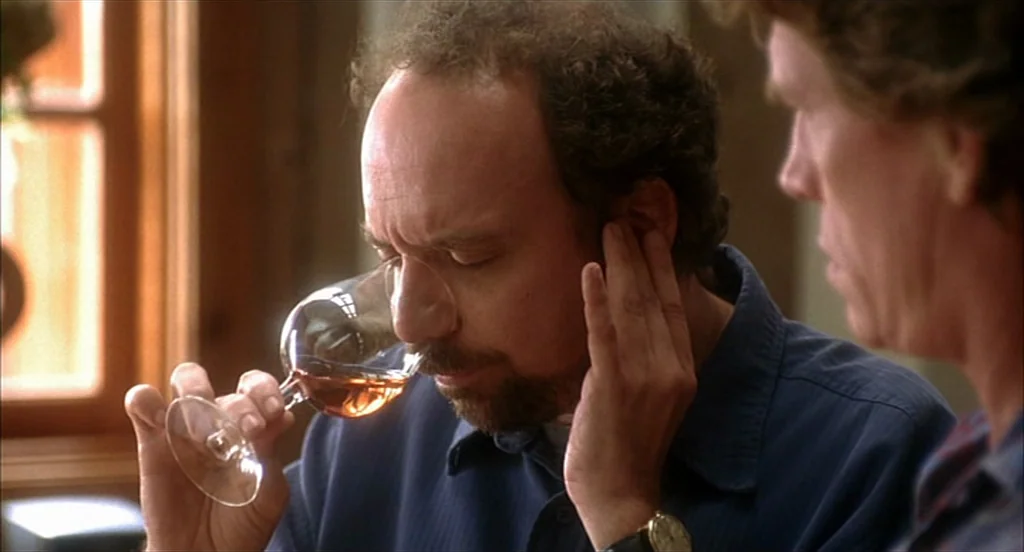 Sideways (2004) movie still: closeup — A man evaluates the scent of wine while a second person observes nearby. Light streams through a large window…