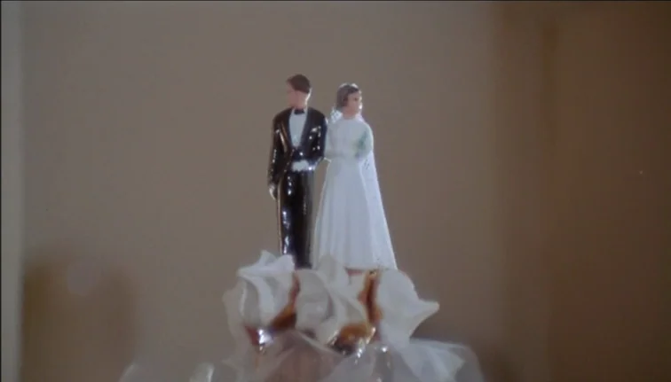 Le Boucher (1970) movie still: closeup — A miniature plastic bride and groom stand atop a frosted wedding cake. The background is a plain, solid,…