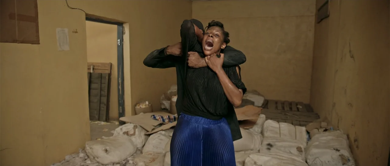 Crossroads (1986) movie still: medium — A windowless room contains stacked white storage sacks and beige unfinished walls. A person in a black shirt…