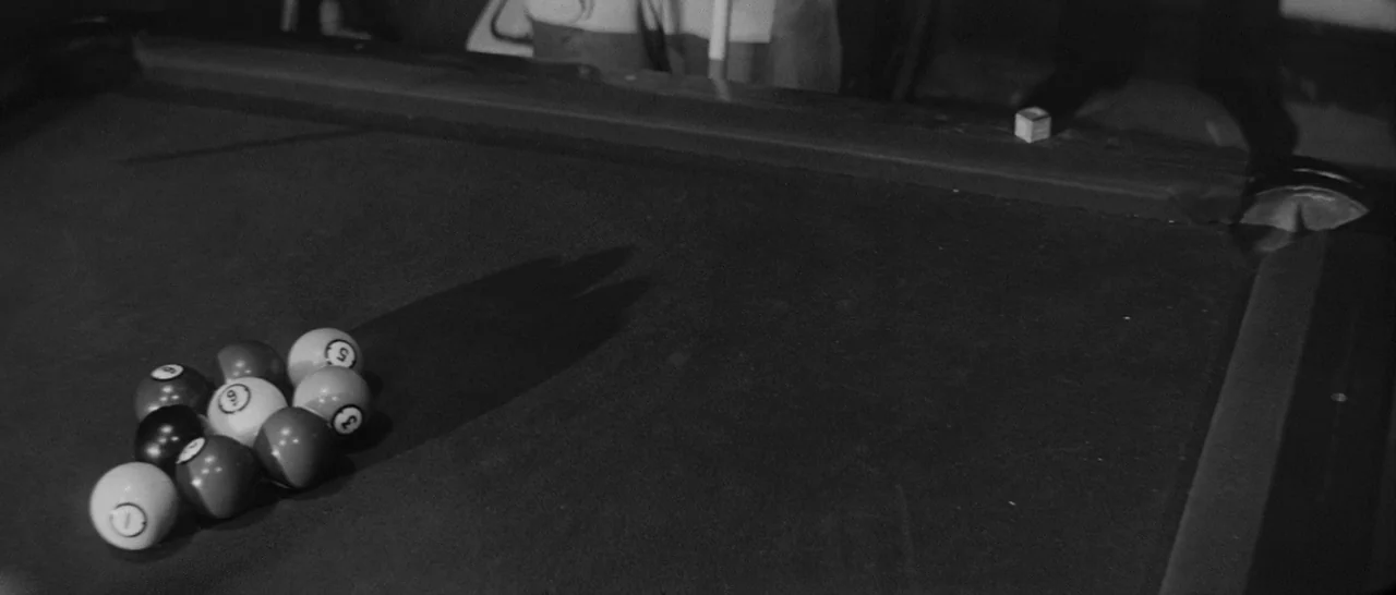 The Hustler (1961) movie still: medium — A dark, felt-covered surface hosts a cluster of arranged billiard balls under low light. A single cube of…