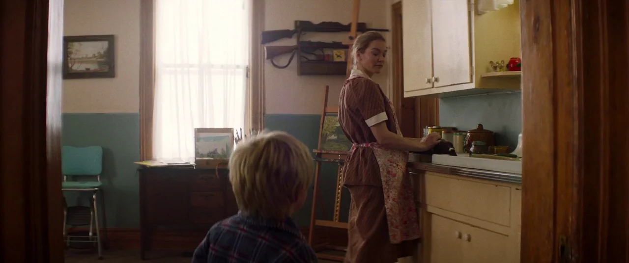 Falling (2020) movie still: medium — A 1950s house interior features a woman at a sink in a small space. Beside her stands a wooden easel and on the…