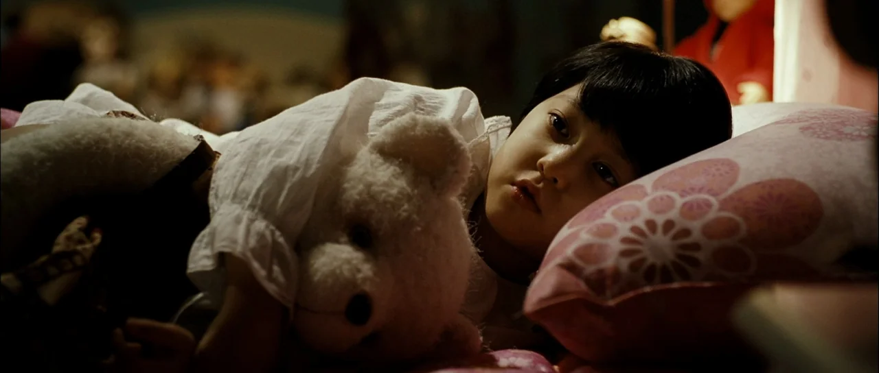 The Housemaid (2010) (2010) movie still: closeup — A dark, out-of-focus bedroom setting with soft lighting on a child. A child with black hair lies…