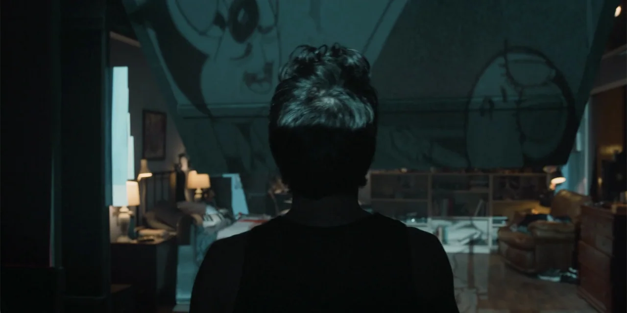 Música (2024) movie still: medium — A cluttered apartment at night with large projected drawings visible on the wall. A man in a dark shirt stands…