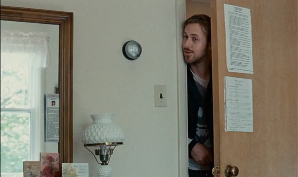 Blue Valentine (2010) movie still: medium — An interior wall with an off-white painted finish features a thermostat and light switch. A man peers…