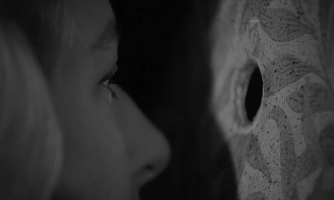 Seance on a Wet Afternoon (1964) movie still: closeup — A dark, textured wall features a small circular hole drilled through the surface. A person's…