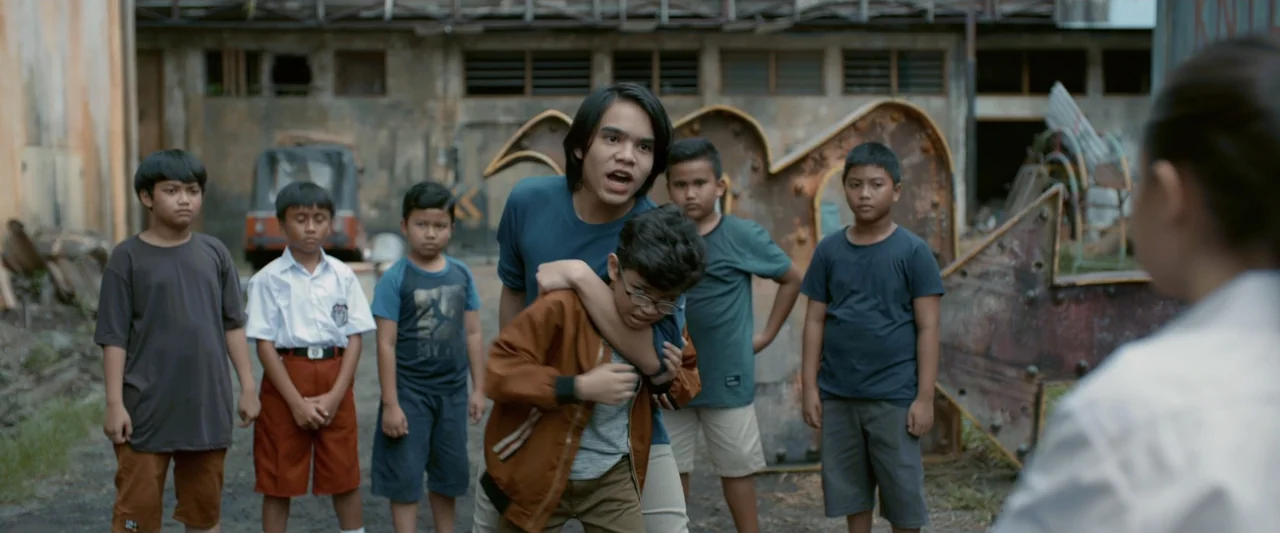The Chanting 3 (2008) movie still: medium — A group of young boys stands in a cluttered outdoor area filled with debris. One teenager aggressively…