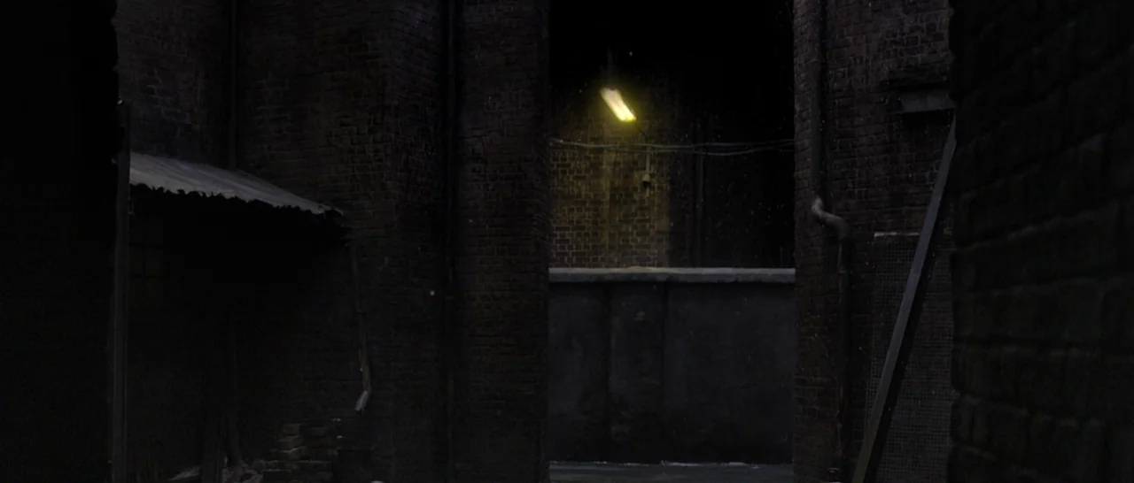 Nymphomaniac Vol 1 (2013) movie still: establishing — A dark, narrow city alley is framed by damp red brick walls. A single flickering yellow…