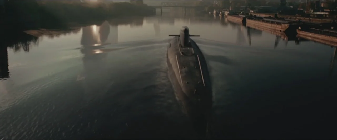 Darkest Hour (2017) movie still: wide — A dark submarine navigates a calm river during the late afternoon. The vessel leaves a wake in the water…