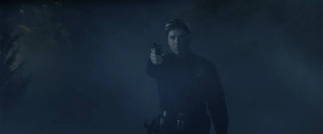 Companion (2025) movie still: medium — A dark, misty outdoor setting obscured by heavy fog and low visibility. A person in a law enforcement uniform…