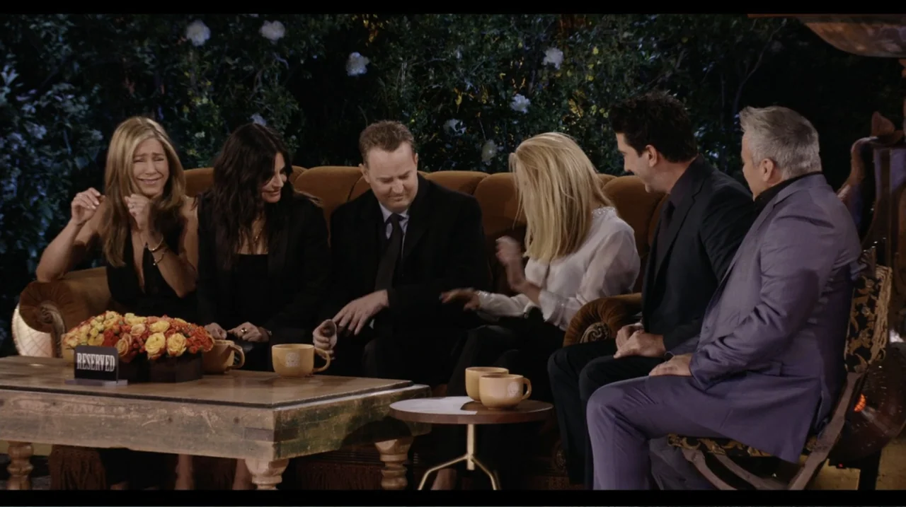 Friends: The Reunion (2021) movie still: medium — Six friends sit on a worn velvet sofa in a brightly lit television studio. They are gathered…