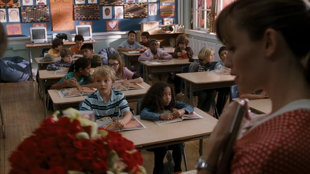 F Valentine's Day (2026) movie still: medium — A primary school room features rows of desks facing the front with colorful artwork displayed. A…