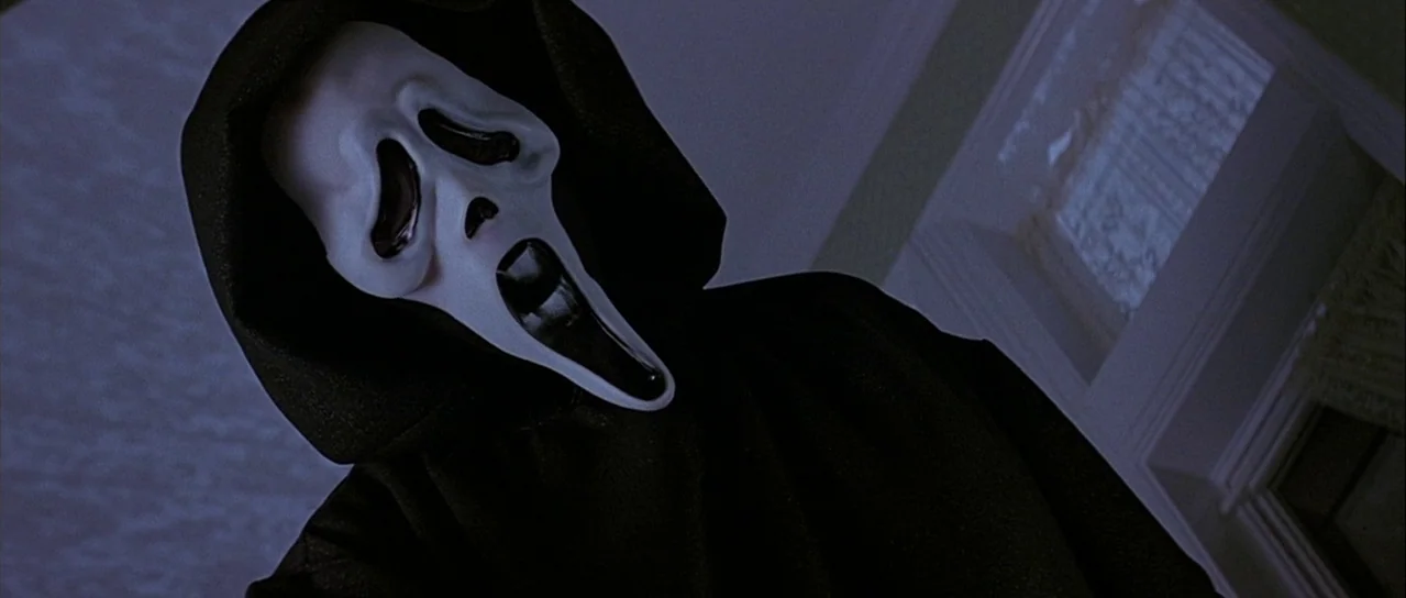 Scream (1996) movie still: closeup — The interior of a house at night with dim blue lighting filling the space. A masked figure in a black hood…