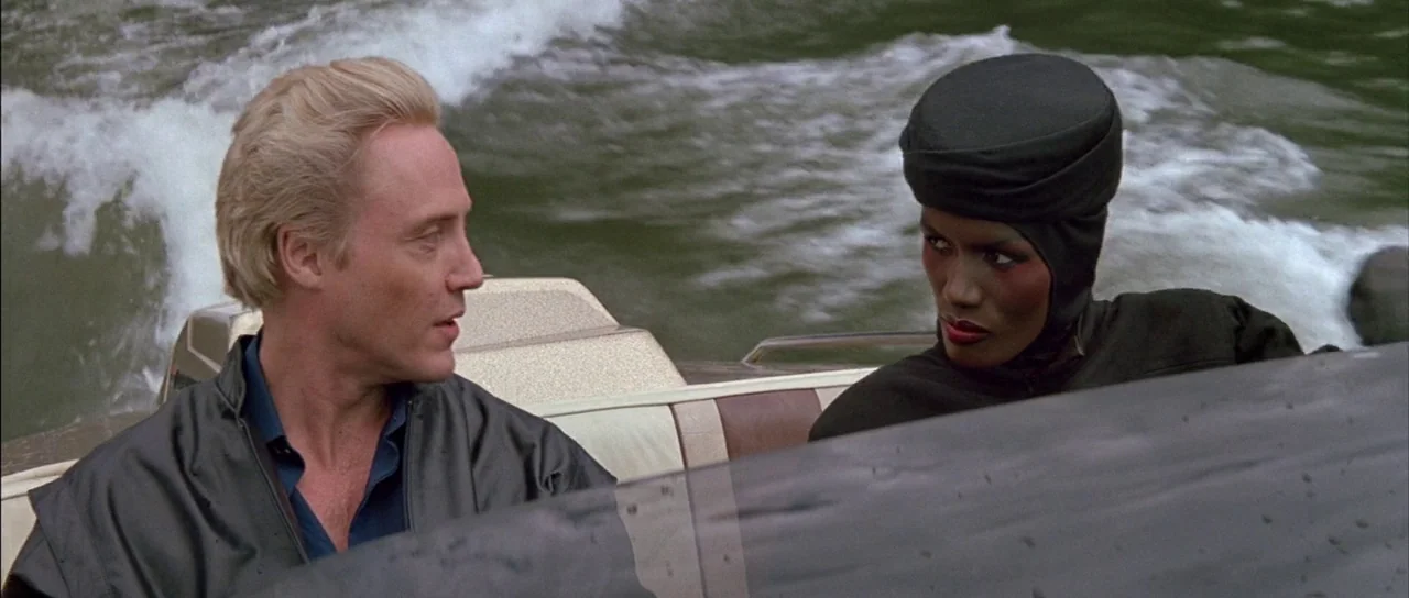 A View to a Kill (1985) movie still: medium — Two individuals ride in a motorboat moving across choppy water. The man and woman sit together in the…