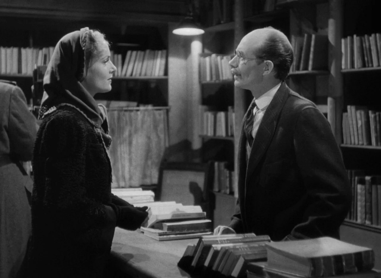 To Be or Not To Be (1942) movie still: medium — A crowded bookstore interior with shelves filled with books lining the walls behind counters. A man…