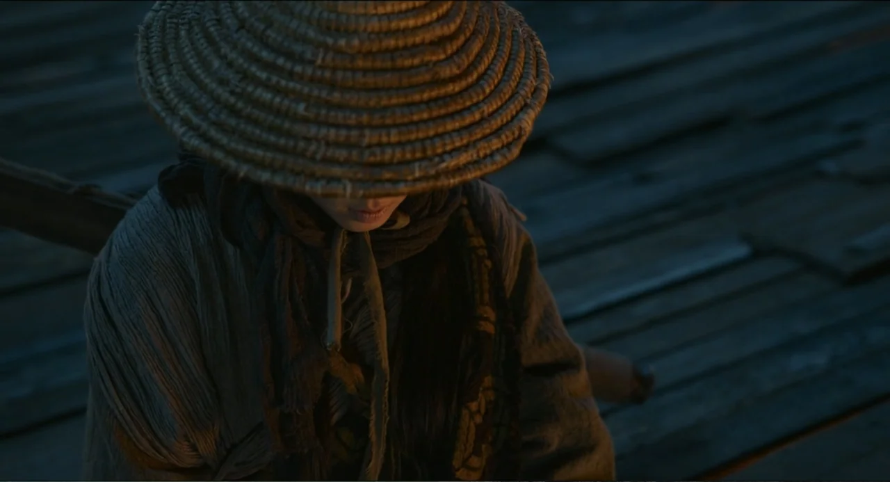 Legends of the Condor Heroes: The Gallants (2025) movie still: medium — A person wearing a large straw hat sits on a dark weathered wooden dock at…