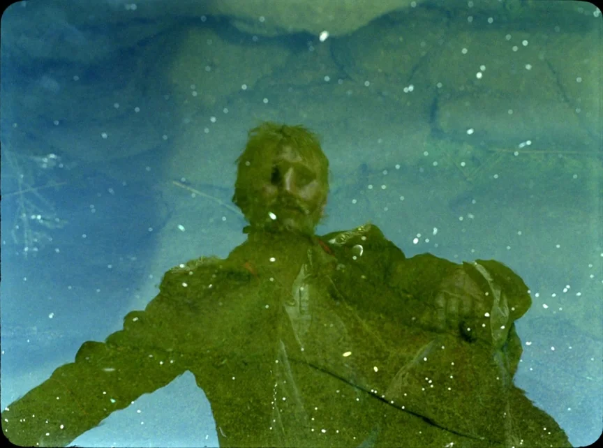 Jauja (2014) movie still: medium — A man's face and upper torso are visible through murky, algae-filled green water. He remains still while…