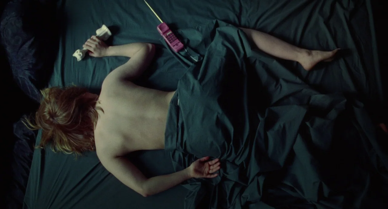What Happened Was… (1994) movie still: fullbody — A dark, wrinkled grey bedsheet covers a flat surface viewed from directly above. A woman lies face…