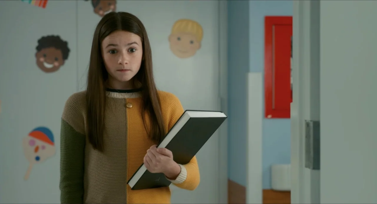 IF (2024) movie still: medium — A school corridor features light blue walls decorated with colorful child-like cartoon stickers. A young girl in a…