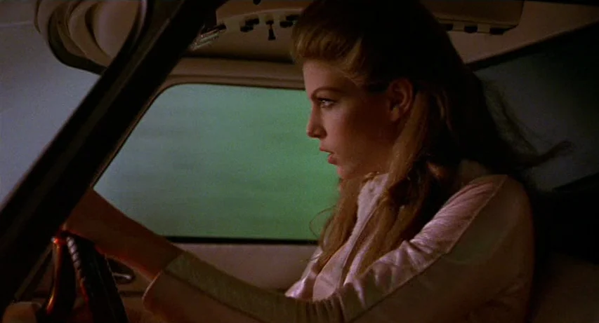 CQ (2001) movie still: medium — The interior of a vehicle at night with a dark green window reflection visible. A young woman with blonde hair holds…