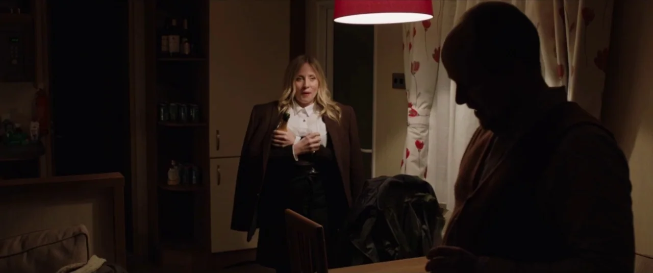 Happy New Year, Colin Burstead (2018) movie still: medium — A dim domestic space features a table and chair under a hanging red lamp. A man stands…