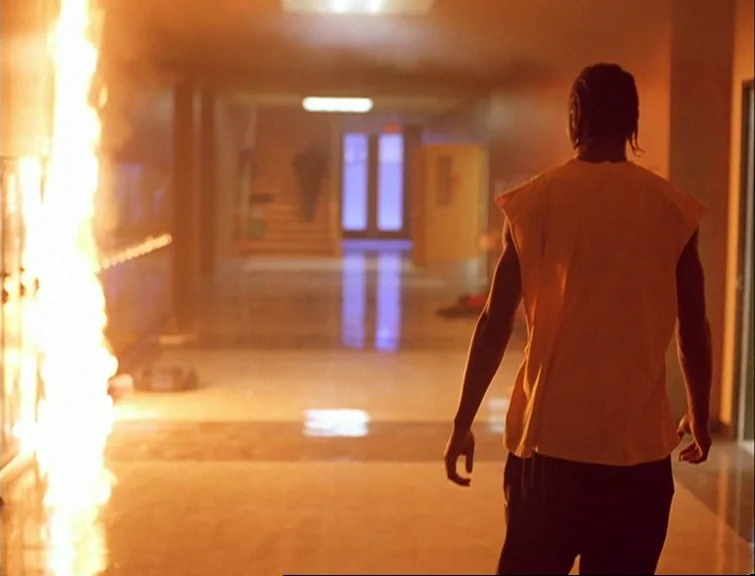 Elephant (2003) movie still: medium — An interior school hallway filled with smoke and firelight. A solitary man walks down the center of the hall…