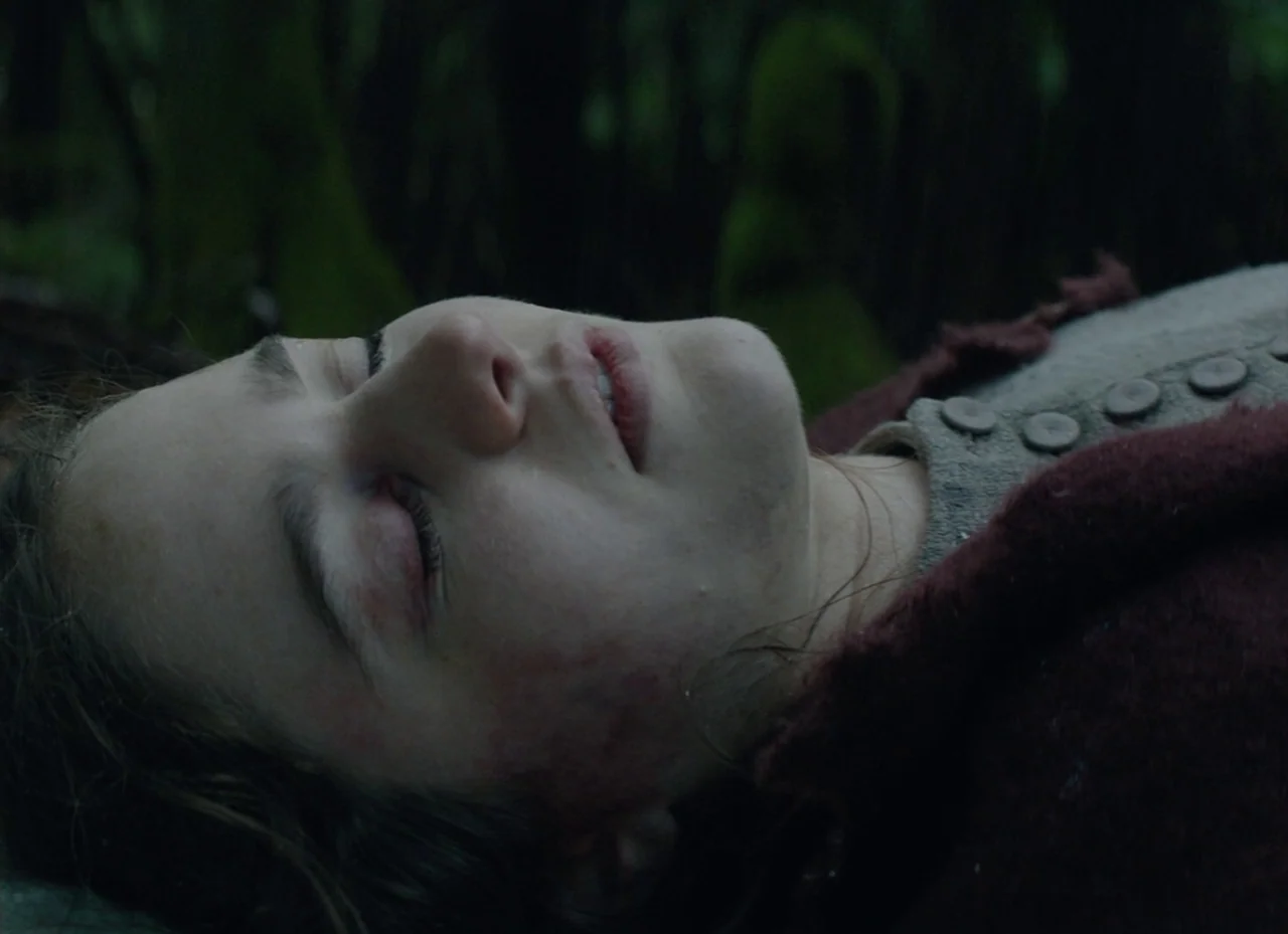 The Nightingale (2018) movie still: closeup — A dark temperate woodland setting with mossy trees and dense ground vegetation. A young woman lies…
