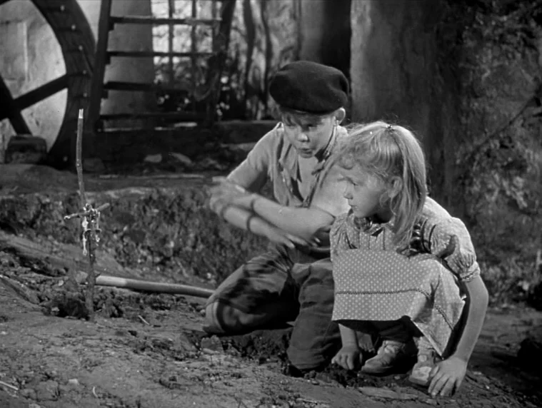 Forbidden Games (1952) movie still: medium — An outdoor area near a water mill features dirt ground and wooden wheel structures. A boy and a girl…