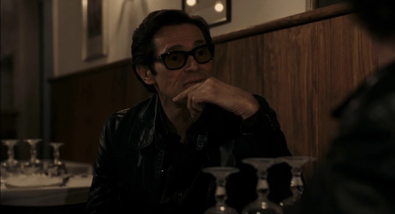 Pasolini (2014) movie still: medium — A dimly lit restaurant booth features wood-paneled walls and a white-clothed table. A man wearing black-rimmed…