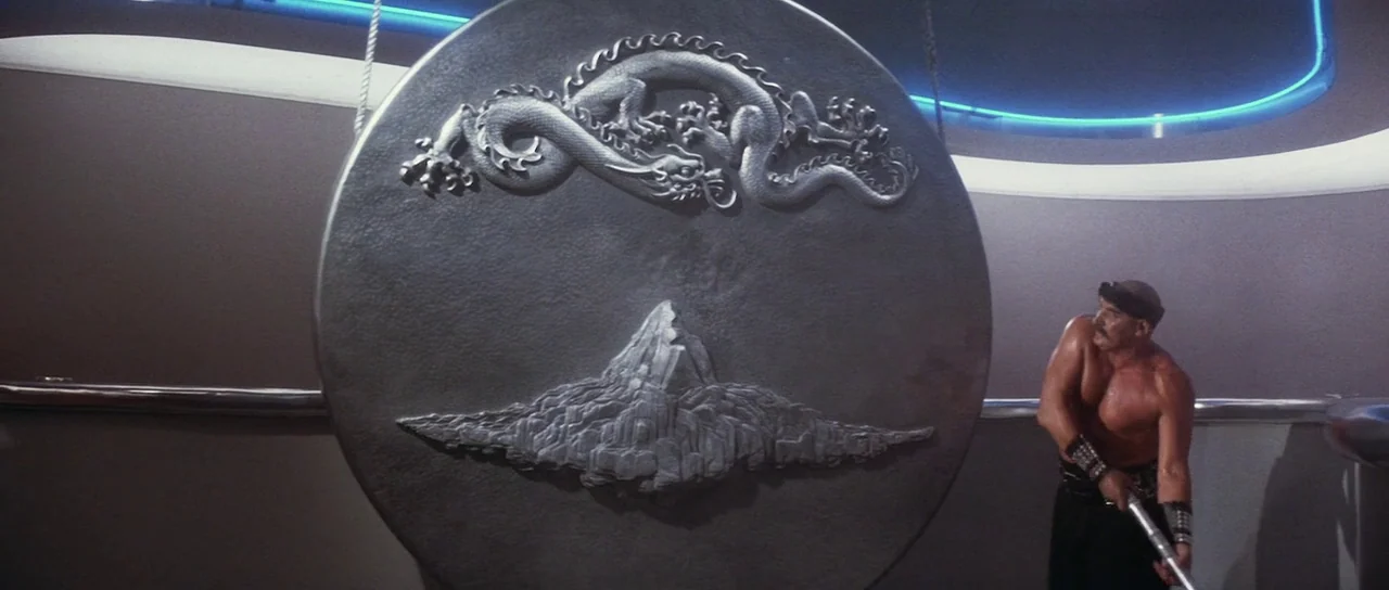 Indiana Jones and the Temple of Doom (1984) movie still: wide — A modern curved room features a large metallic gong embossed with a dragon and…