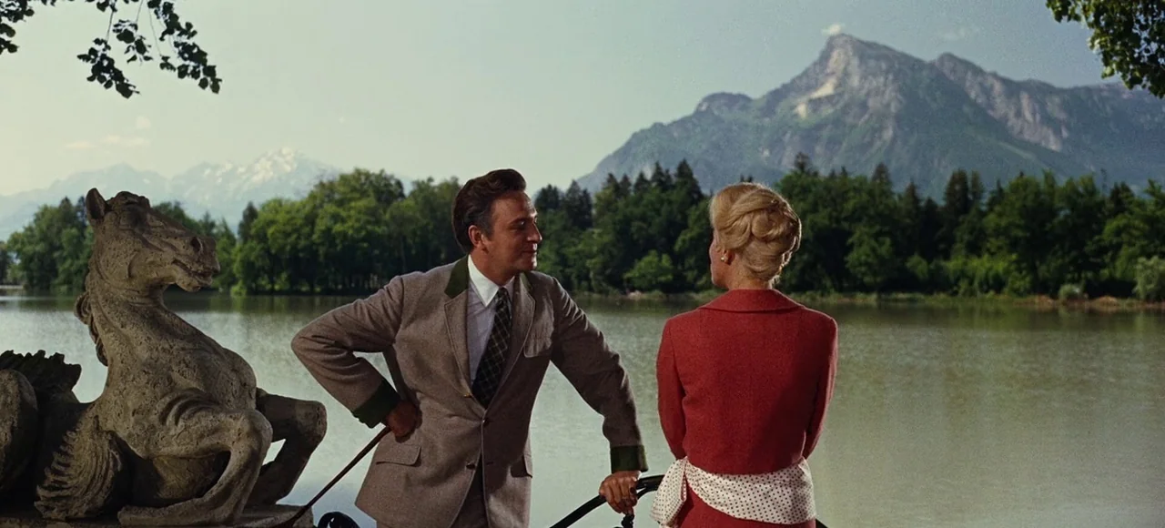 The Sound of Music (1965) movie still: medium — A man and woman converse beside a calm lake with mountains in the background. A decorative stone…