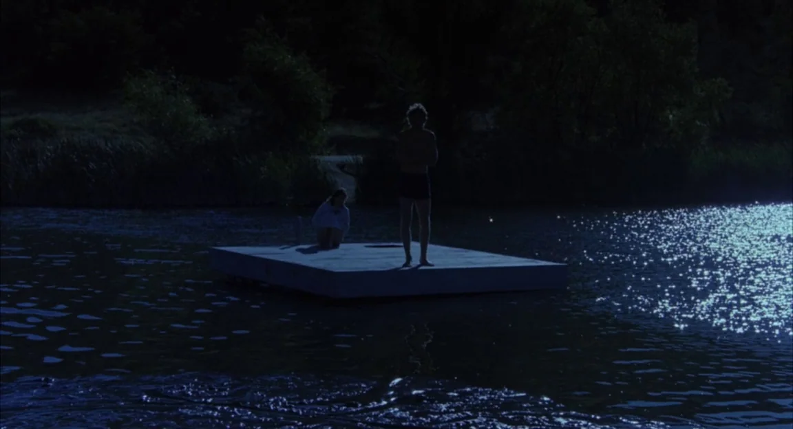 Creepshow 2 (1987) movie still: wide — A dark, still lake surrounds a small floating platform during the night. A man stands upright on the raft…