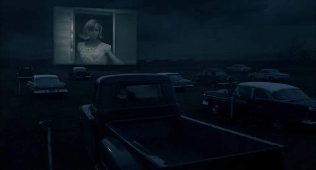 Brokeback Mountain (2005) movie still: wide — A dark, expansive field filled with vintage cars parked before a large cinema screen. A black and…