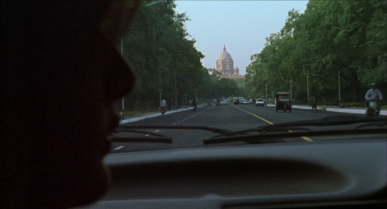 Monsoon Wedding (2001) movie still: wide — A view from inside a car driving down a wide, tree-lined boulevard. In the distance, a large domed…