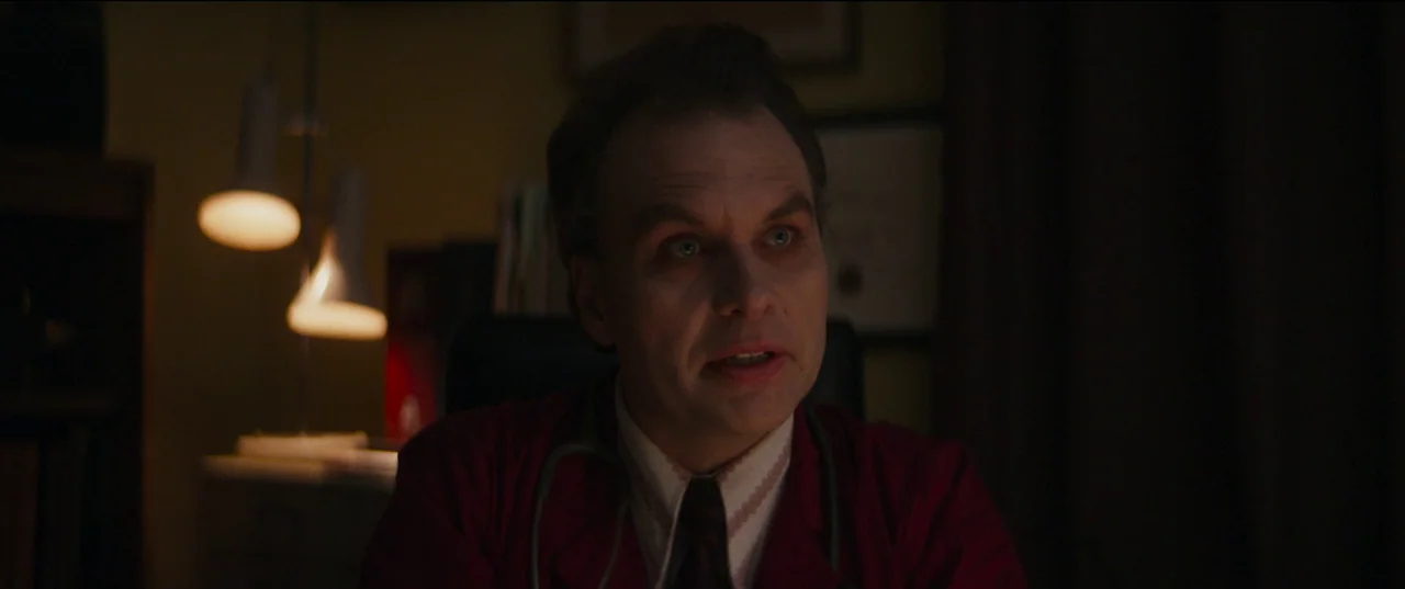 Humanist Vampire Seeking Consenting Suicidal Person (2023) movie still: closeup — A dimly lit professional office with a desk lamp providing the…