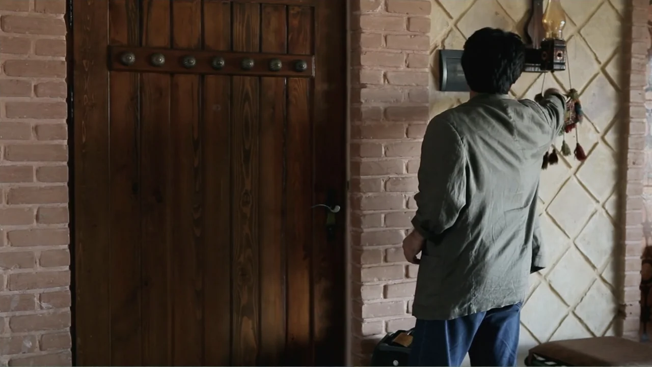 Closed Curtain (2013) movie still: medium — An interior space features a heavy wooden door mounted in a brick wall. A man in a green jacket adjusts…