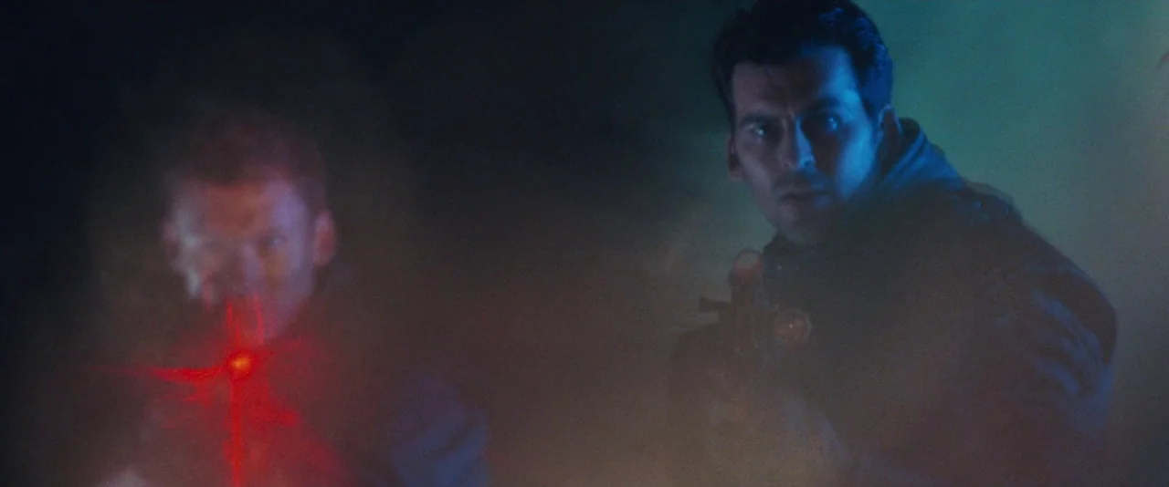 Resident Evil: Apocalypse (2004) movie still: medium — Two men stand in a dark, thick-smoke-filled environment lit by contrasting light. They aim…