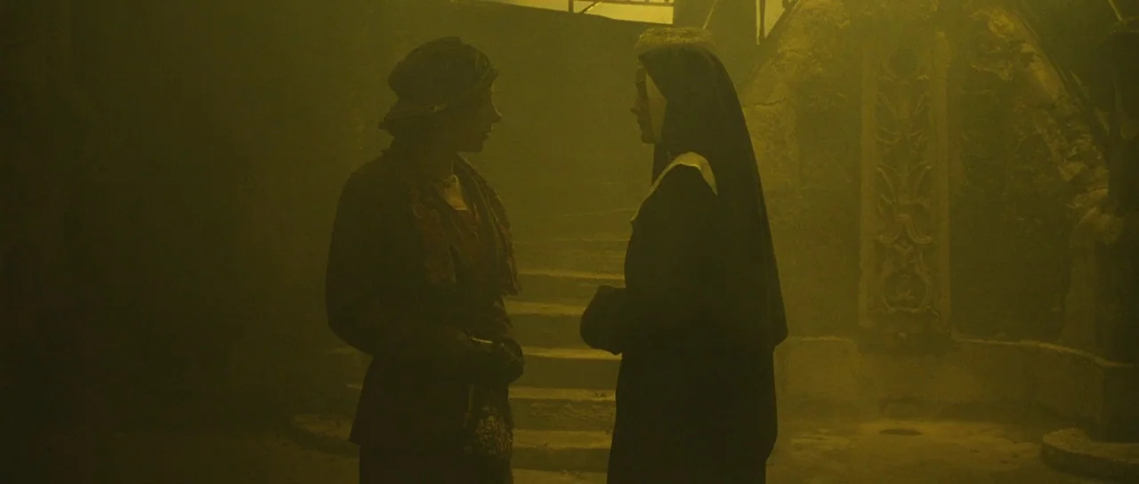 A Very Long Engagement (2004) movie still: medium — A dark, atmospheric stone stairwell is filled with dense yellow smoke or haze. A woman in a hat…