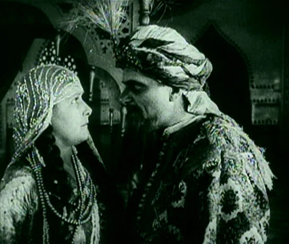 Destiny (1921) movie still: medium — A dimly lit room features ornate arched doorways and traditional architectural details in the background. A man…