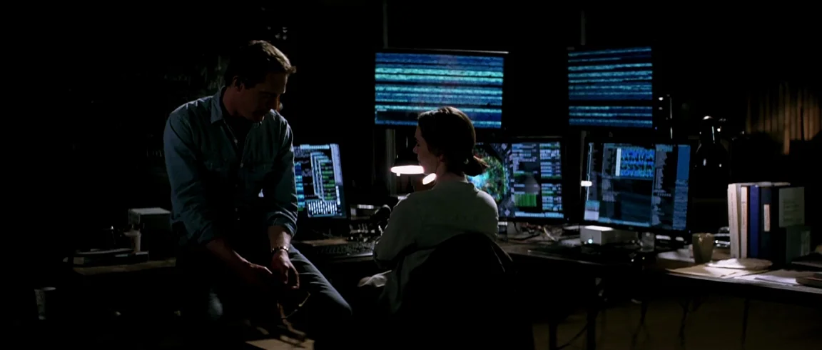 Transcendence (2014) movie still: medium — A dimly lit room filled with multiple glowing computer monitors and technical equipment. A man and a…