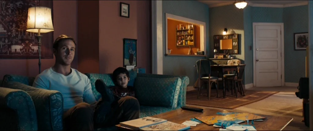 Drive (2011) movie still: medium — An interior living room features a blue patterned sofa, a wooden coffee table, and walls painted in muted teal…