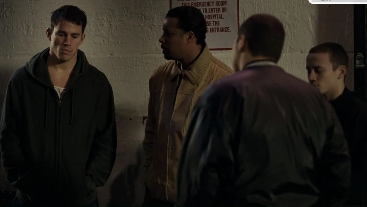 Fighting (2009) movie still: medium — Four men congregate in a dimly lit exterior space near a concrete wall. A red and white emergency sign is…